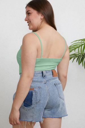 a woman wearing a green tank top and denim shorts