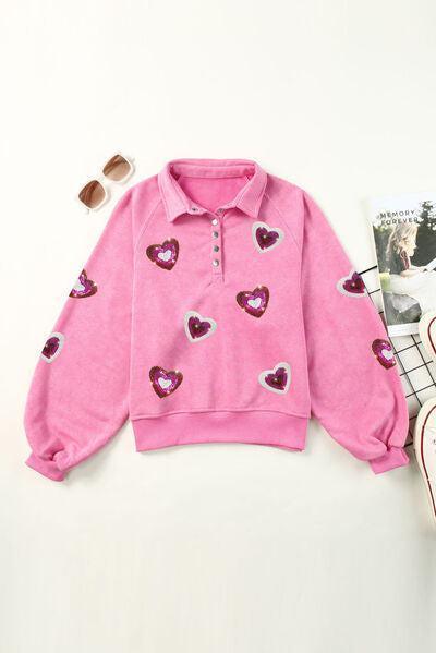 a pink sweater with hearts on it next to a skateboard