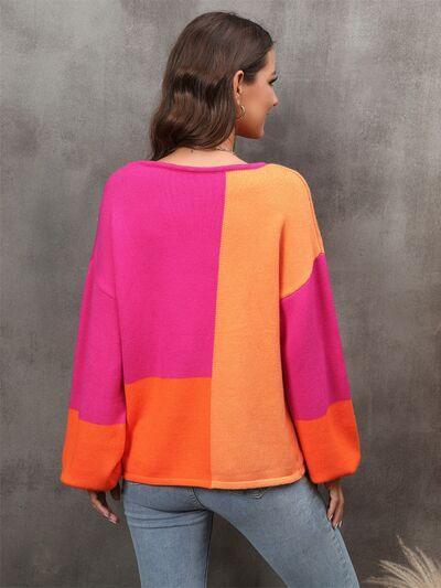 a woman standing in front of a wall wearing an orange and pink sweater