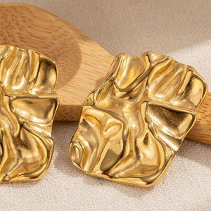 a pair of gold earrings sitting on top of a wooden paddle