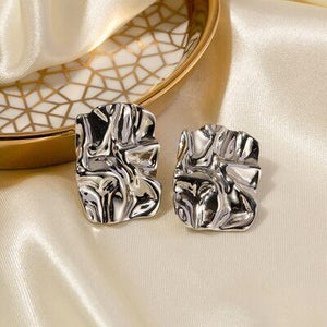 a pair of silver square earrings sitting on top of a white cloth