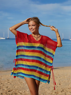 a woman standing on a beach holding a colorful blanket over her head