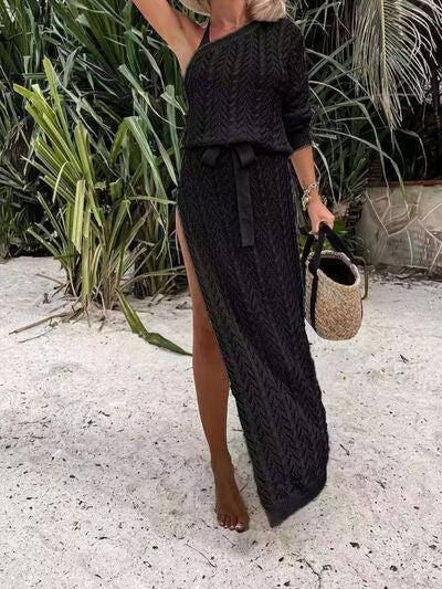 a woman in a black sweater dress standing on a beach