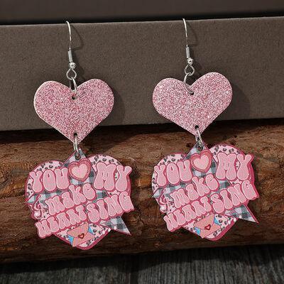 a pair of pink heart shaped earrings hanging from a piece of wood