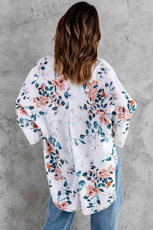 a woman standing against a wall wearing a white floral shirt