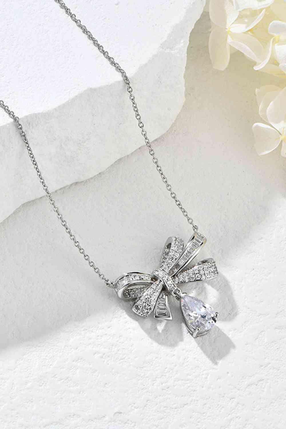 a necklace with a bow on it next to a flower