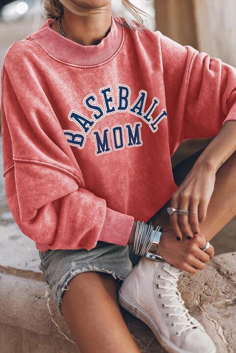 a woman sitting on a ledge wearing a baseball mom sweatshirt