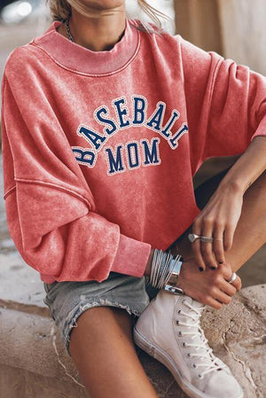 a woman sitting on a ledge wearing a baseball mom sweatshirt