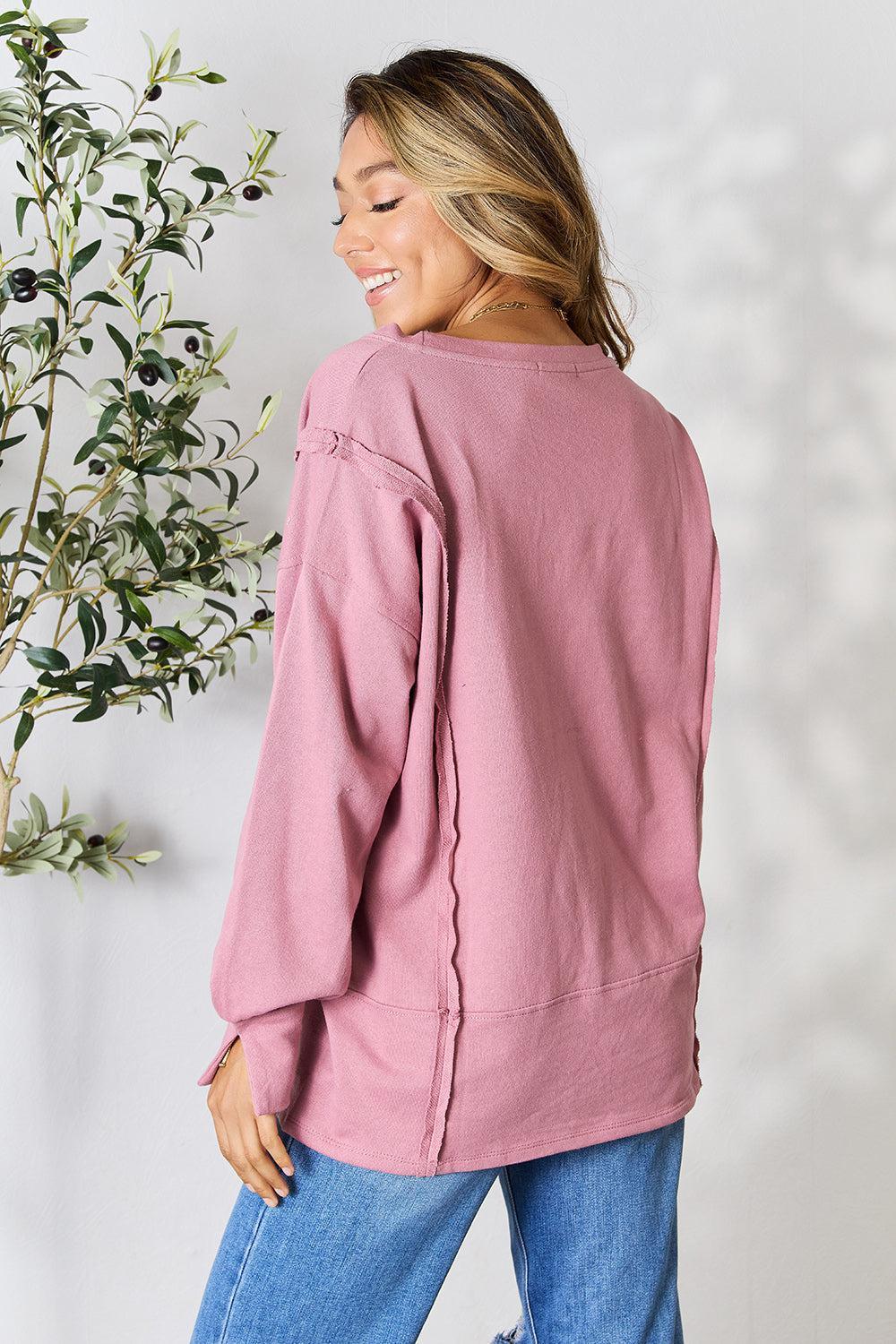 a woman standing next to a plant wearing a pink sweater