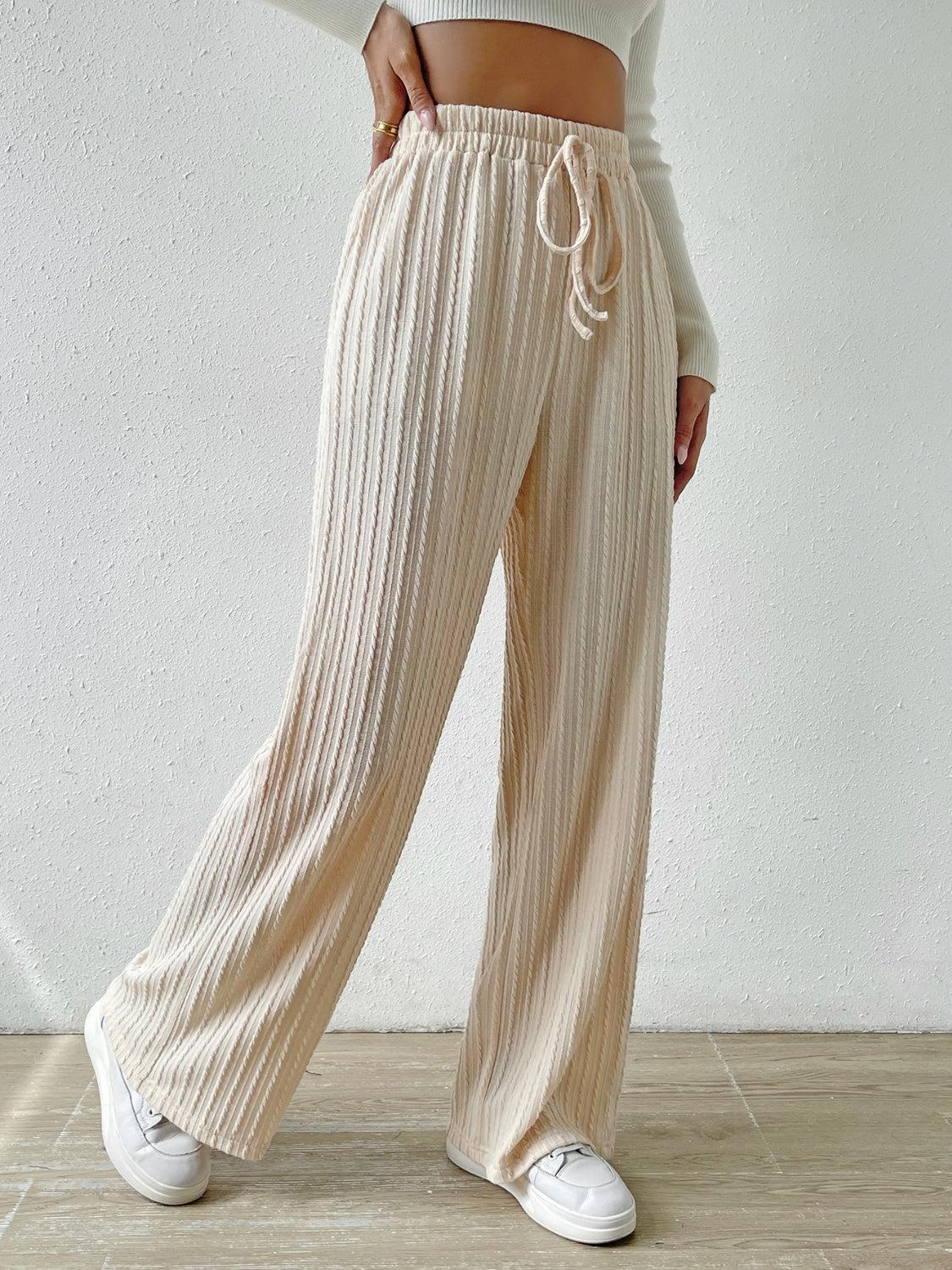 a woman in a white top and pleated pants