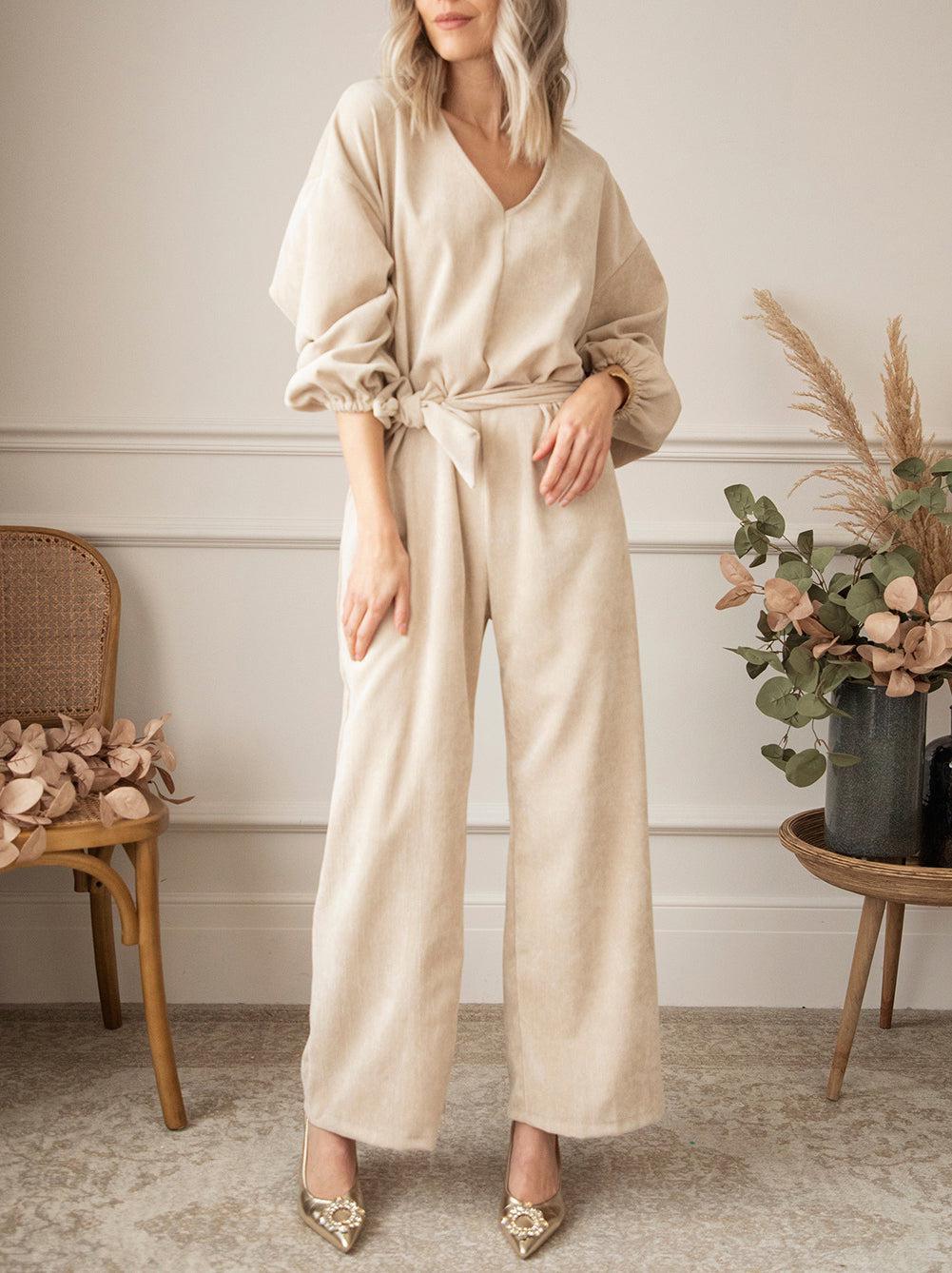 a woman standing in a room wearing a beige jumpsuit