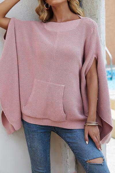 a woman leaning against a wall wearing a pink sweater
