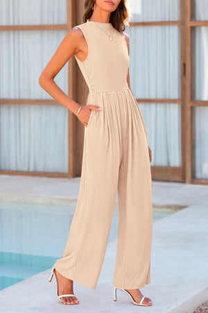 a woman standing next to a pool wearing a tan jumpsuit