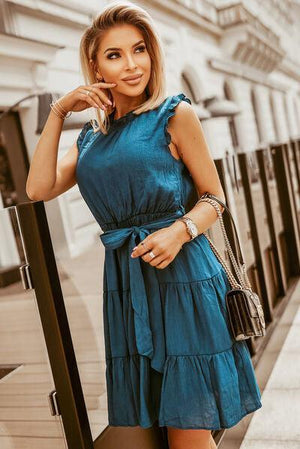 a woman in a blue dress leaning against a rail