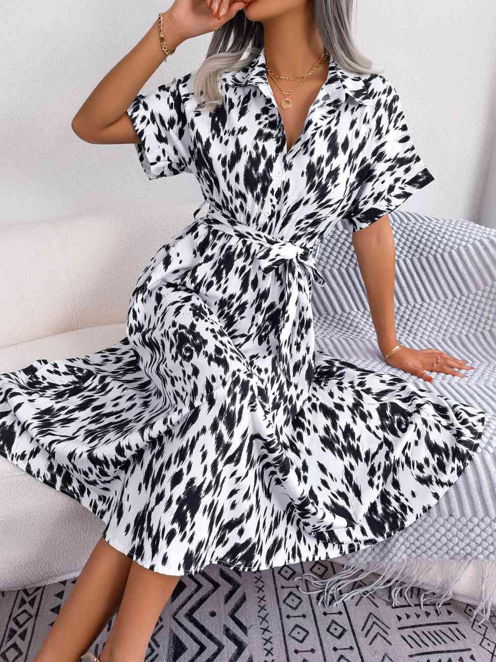 a woman sitting on a bed wearing a black and white dress