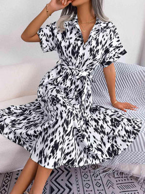 a woman sitting on a bed wearing a black and white dress