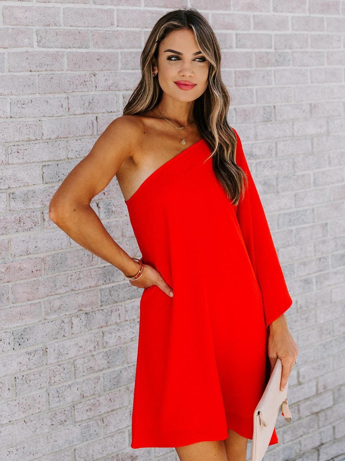 a woman standing in front of a brick wall wearing a red dress