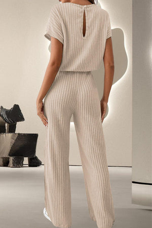 a woman standing in a white room wearing a beige jumpsuit