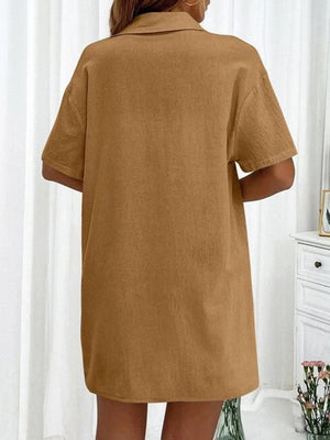 a woman standing in front of a mirror wearing a brown shirt dress