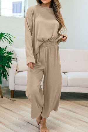 a woman standing in a living room wearing a tan jumpsuit