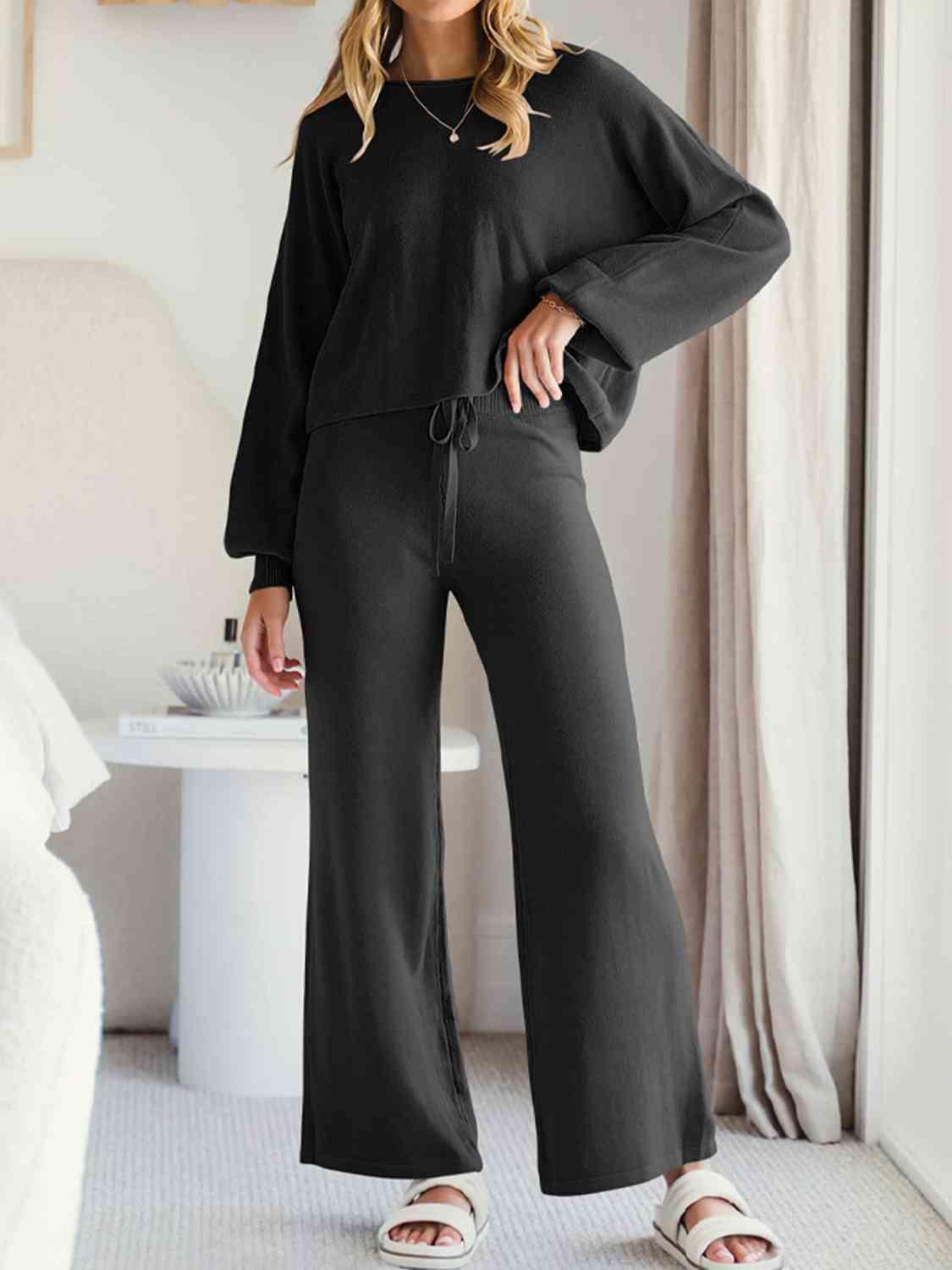 a woman wearing a black top and wide legged pants