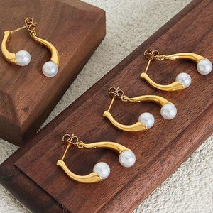 a pair of gold and pearl earrings on a wooden stand