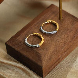 a pair of gold and silver hoop earrings on a wooden stand