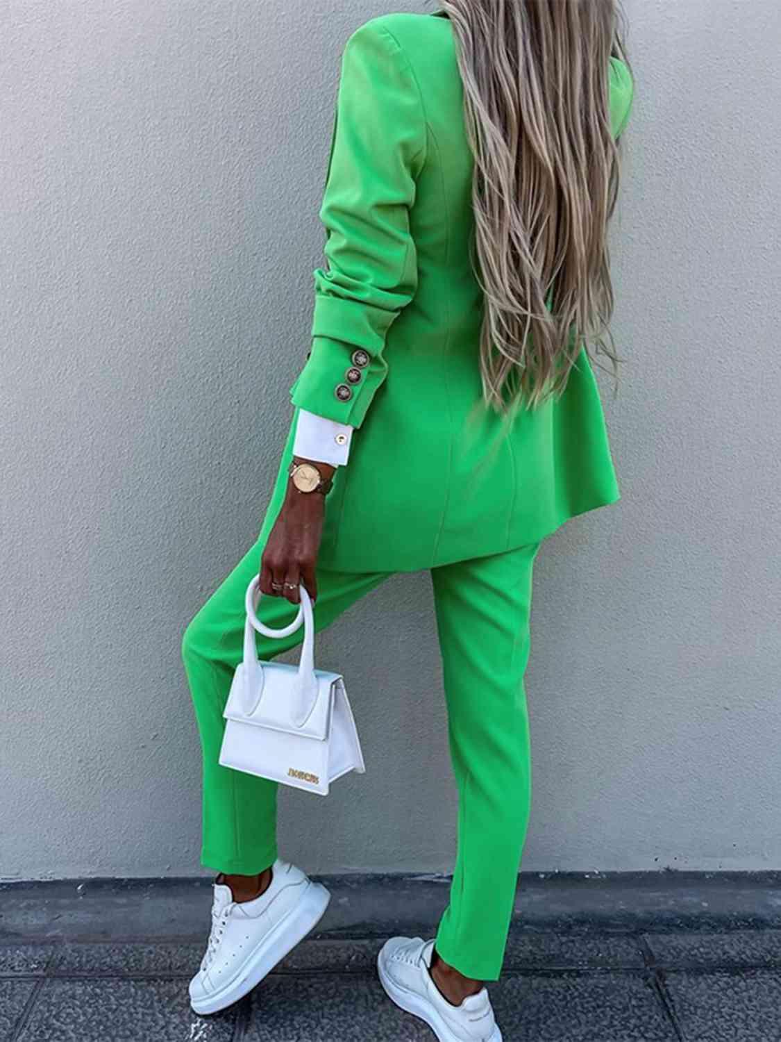 a woman in a green suit leaning against a wall