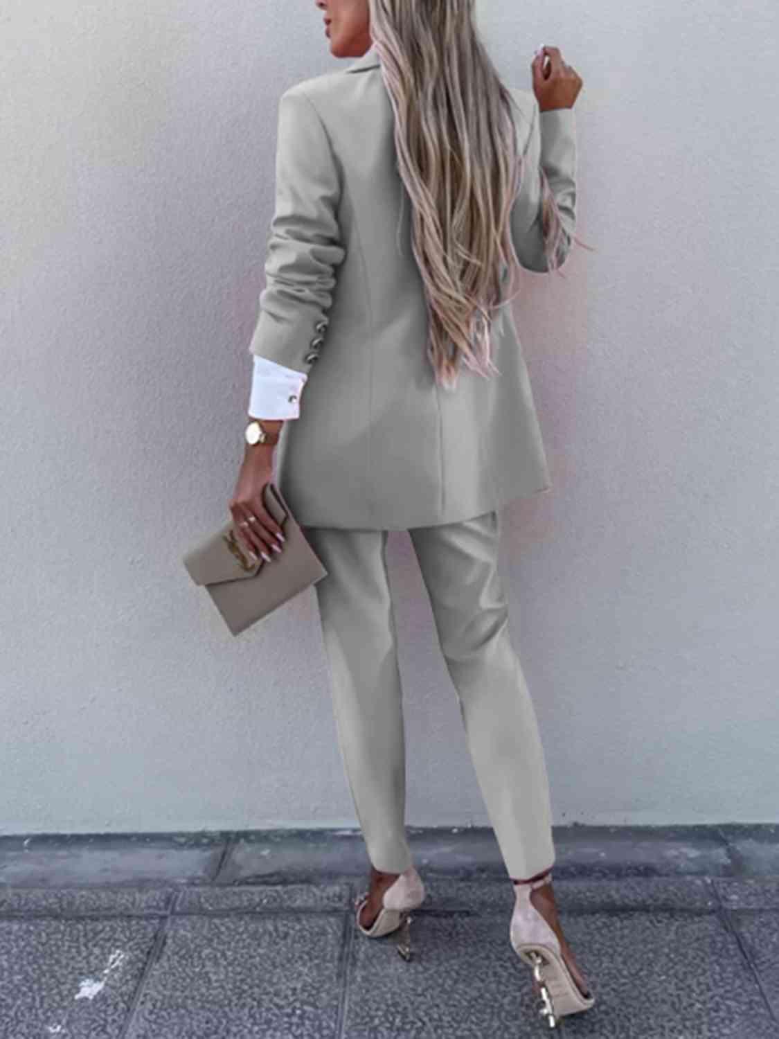 a woman in a suit and heels standing against a wall