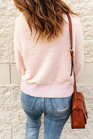 a woman in a pink sweater and jeans is holding a brown purse