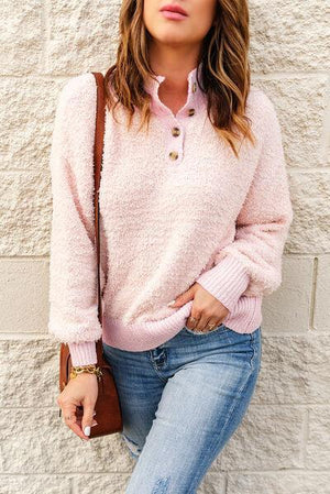 a woman leaning against a wall wearing a pink sweater and jeans