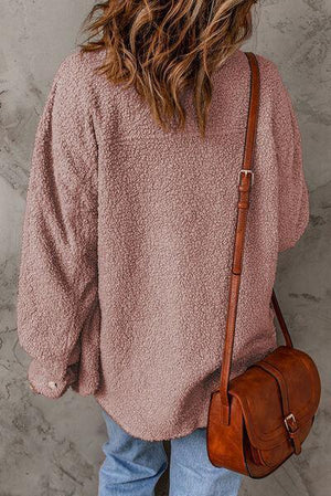 a woman in a pink sweater is holding a brown bag