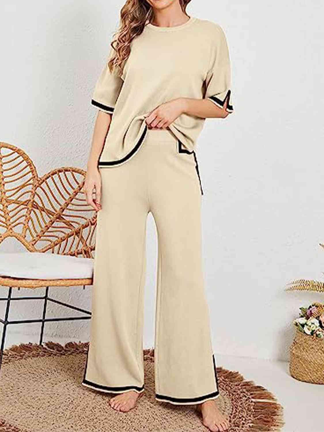 a woman standing in a room wearing a beige top and wide legged pants
