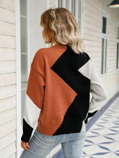 a woman standing on a porch wearing an orange and black sweater