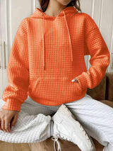 a woman sitting on a couch wearing an orange hoodie