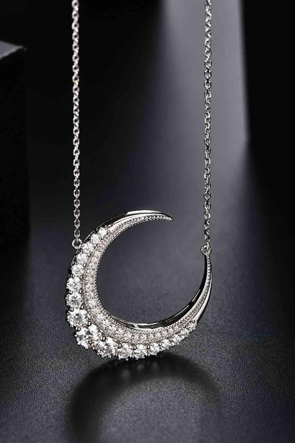 a diamond crescent necklace on a black surface