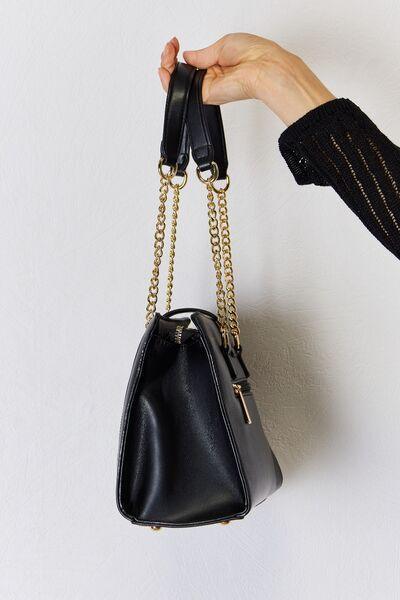 a hand holding a black purse with a gold chain
