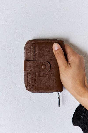 a hand holding a brown wallet on top of a white wall