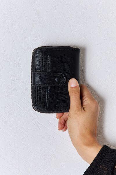 a hand holding a black wallet on a white wall