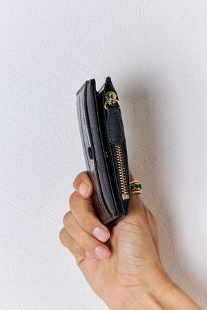 a hand holding a black purse with a gold zipper