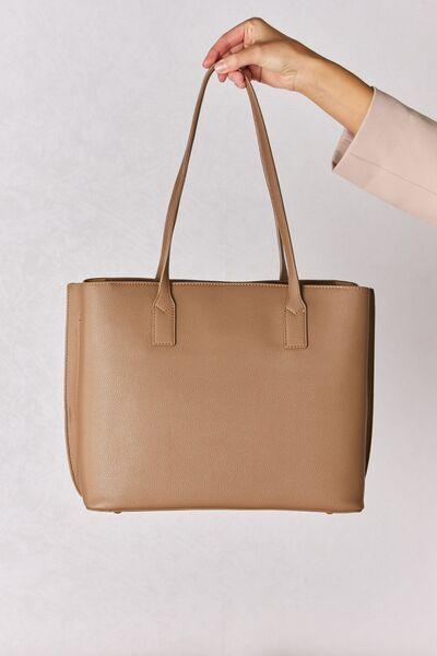 a hand holding a tan leather tote bag