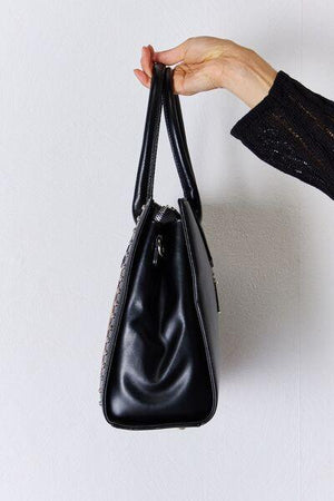 a hand holding a black purse on a white wall