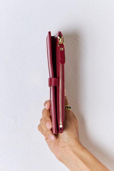 a hand holding a red purse with a gold zipper