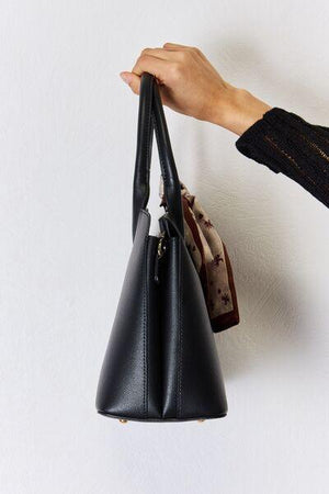 a hand holding a black purse on a white wall