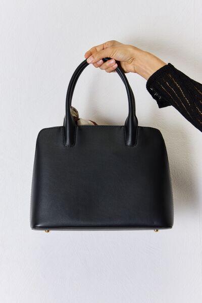 a hand holding a black purse on a white wall