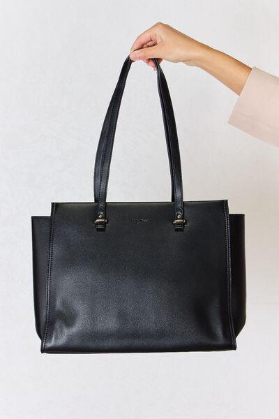 a hand holding a black leather tote bag