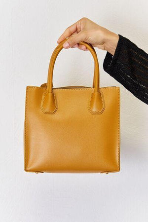 a hand holding a tan leather handbag against a white wall