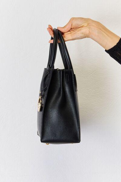 a hand holding a black purse against a white wall