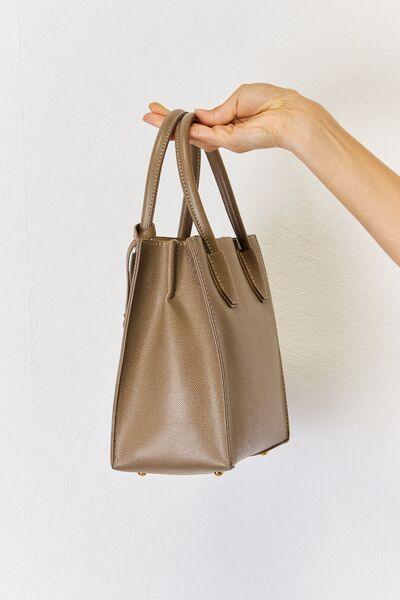 a hand holding a brown purse in front of a white wall