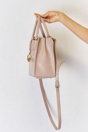a hand holding a beige purse on a white wall